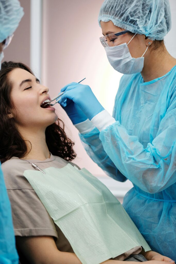 Dentist in protective gear examining a woman's teeth during a dental clinic visit.